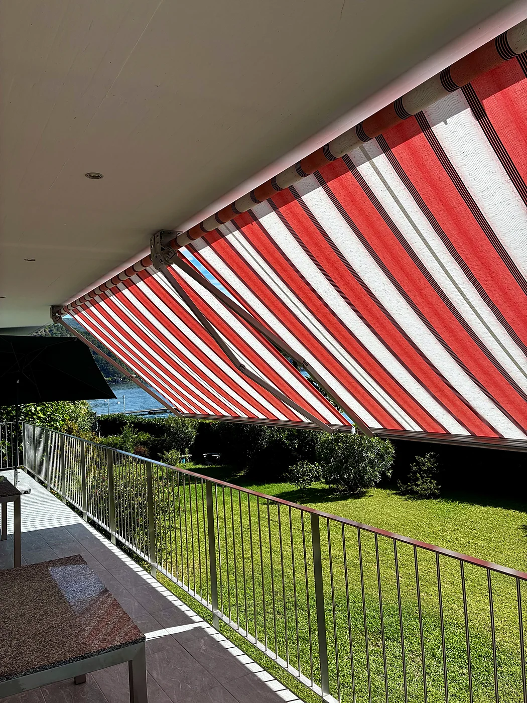 Tenda Lario a righe rosse e bianche aperta su un terrazzo affacciato sul lago