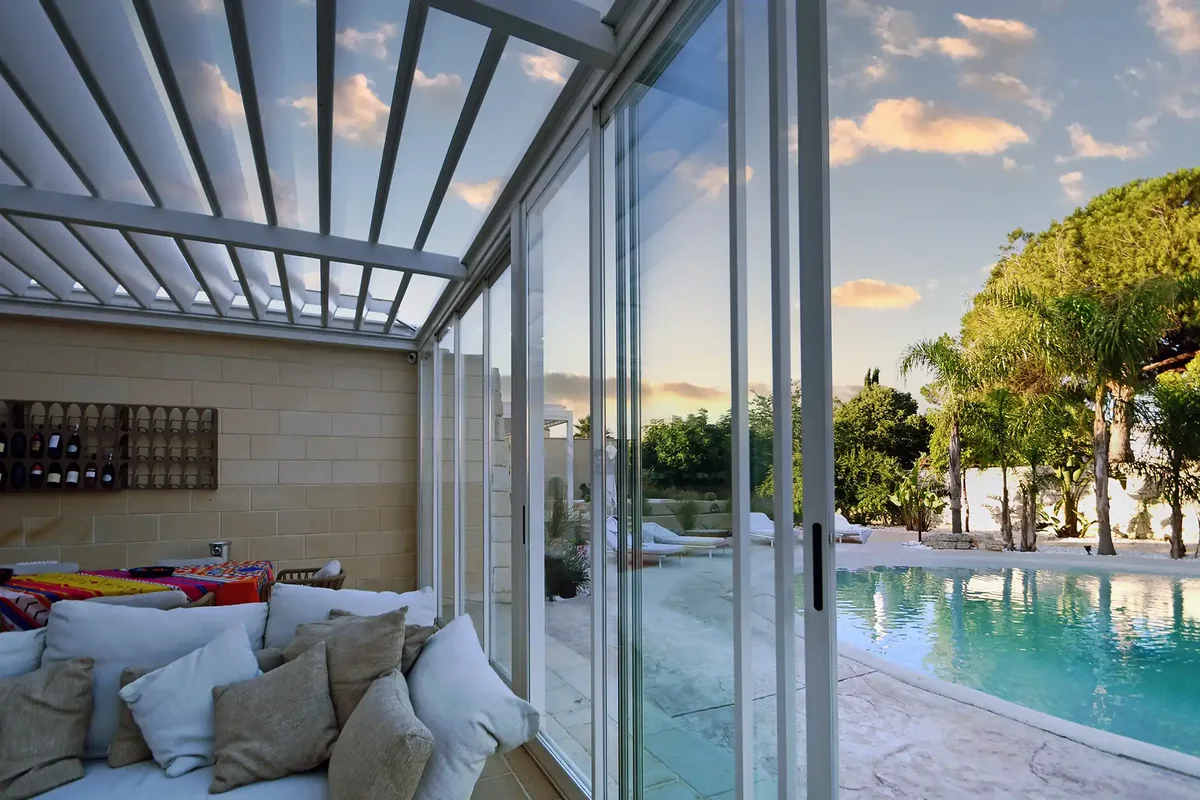 Salotto sotto pergola chiusa da vetrate, piscina fuori